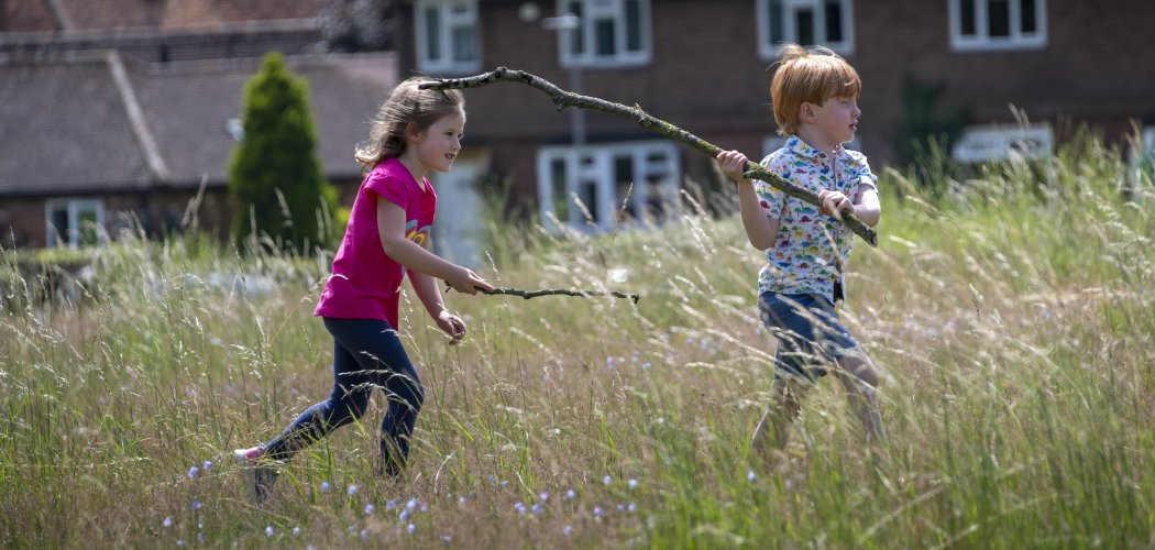 Photo of 2 children carrying sticks playing in the long grass of the wildflower meadow